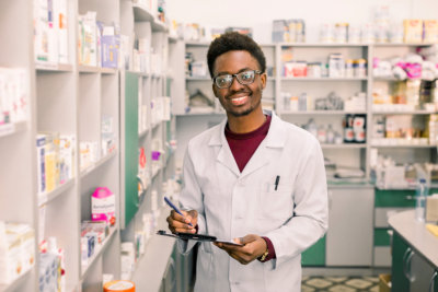 Smiling African American man pharmacist or Chemist Writing On Clipboard While standing in interior of pharmacy