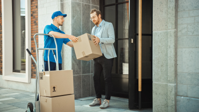 Delivery Man Pushes Hand Truck Trolley Full of Cardboard Boxes Hands Package to a Customer