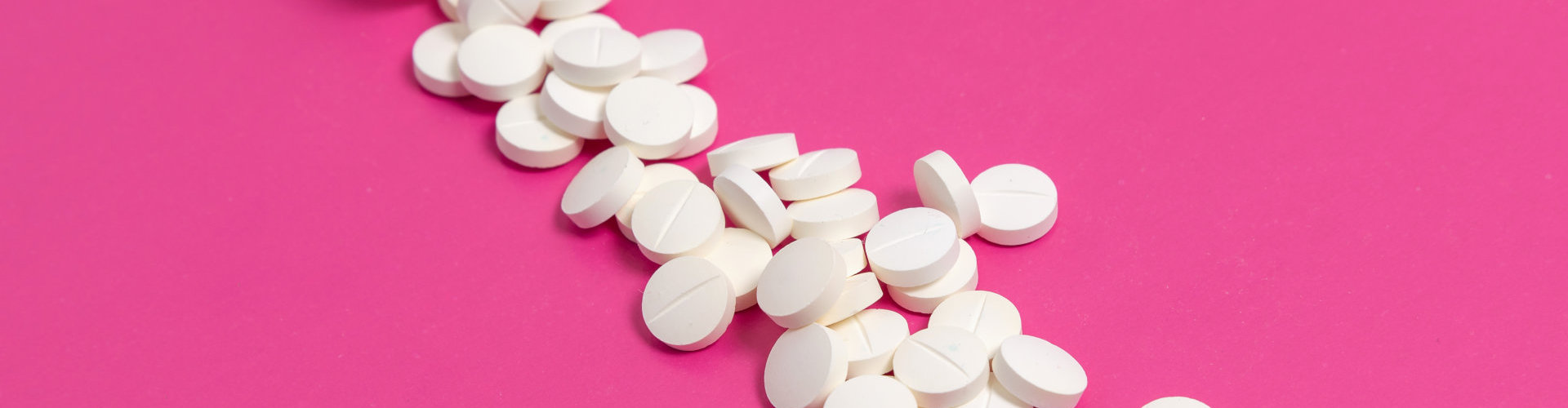 Circle pills drugs or tablets spilling out of a white plastic medicine bottle on pink background