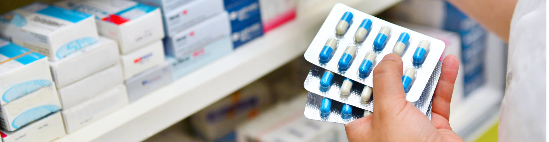 Pharmacist holding medicine box and capsule pack in pharmacy drugstore.